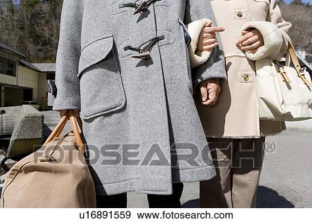 Stock Photo - Senior couple walking down the street, holding bags, arm in arm. Fotosearch