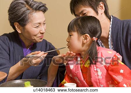Stock Image - Senior woman feeding granddaughter, smiling. Fotosearch