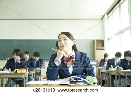 Stock Image - High school students in classroom, girl resting chin on hand. Fotosearch