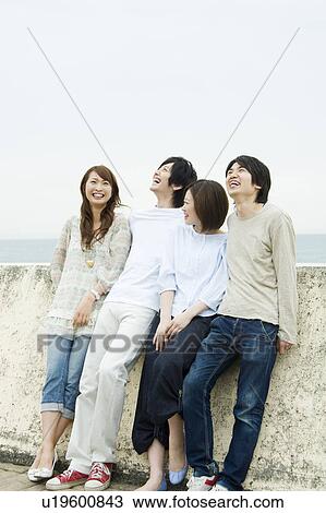 Stock Image - Group of young people leaning on breakwater. Fotosearch