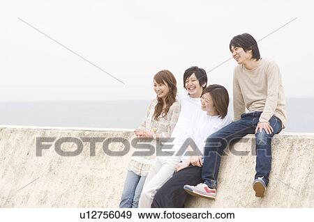 Stock Photo - Group of young people leaning on breakwater. Fotosearch