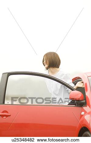 Stock Image - Young woman getting out of a car. Fotosearch
