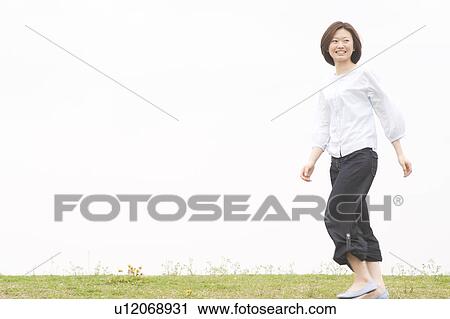 Stock Image - Young woman walking on grass. Fotosearch