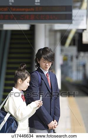 Picture - High school students waiting for the train at platform, girl holding a mobile phone. Fotosearch