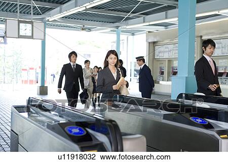 Stock Image - People walking through automatic ticket wicket at station. Fotosearch