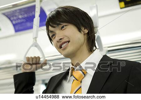 Stock Photo - Young man hanging on to strap, smiling. Fotosearch
