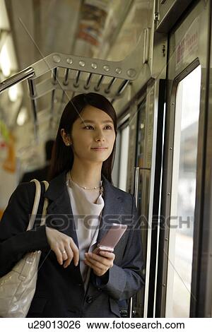 Stock Photograph - Young woman standing beside the door on the train, holding a mobile phone. Fotosearch