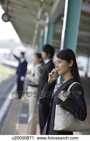 Stock Image - Young woman using mobile phone at platform, differential focus. Fotosearch