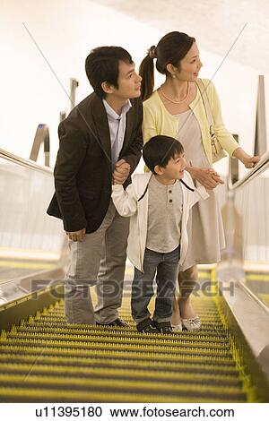 Stock Image - Son and Two Parent Ridding on Escalator in Department Store. Fotosearch