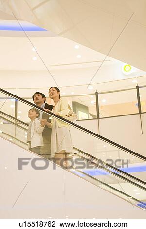 Stock Image - Son and Two Parent Ridding on Escalator in Department Store. Fotosearch