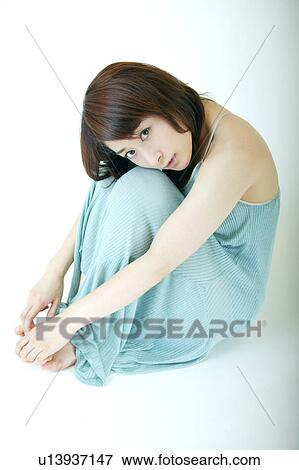 Stock Photo - A young woman hugging her knees. Fotosearch