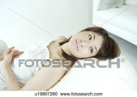 A young woman sitting on a sofa View Large Photo Image Stock Image - A young woman sitting on a sofa. Fotosearch