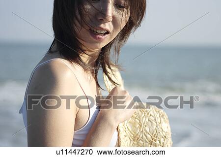 Stock Image - A young woman holding a hat in beach. Fotosearch