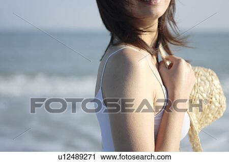 Stock Image - A young woman holding a hat in beach. Fotosearch