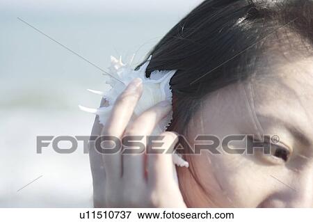 Stock Photo - A young woman listening a shell. Fotosearch