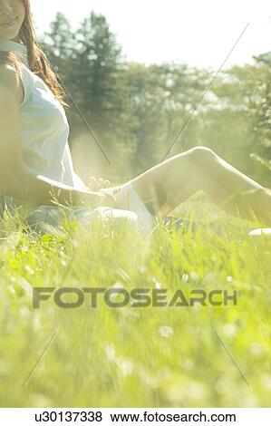 Stock Photo - A young woman sitting on a lawn. Fotosearch
