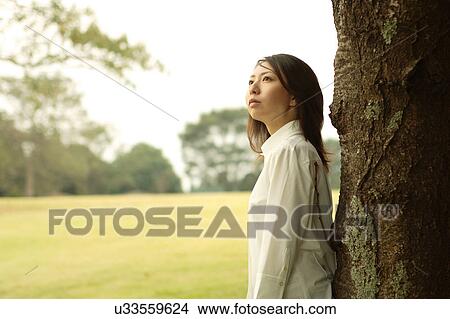 Picture - A young woman standing under a tree. Fotosearch