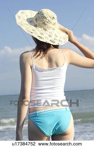Stock Image - A young woman wearing a hat in beach, rear view. Fotosearch