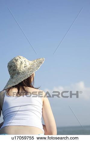Stock Photography - A young woman wearing a hat in beach, rear view. Fotosearch