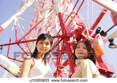 Stock Image - Two women standing in front of Ferris Wheel. Fotosearch