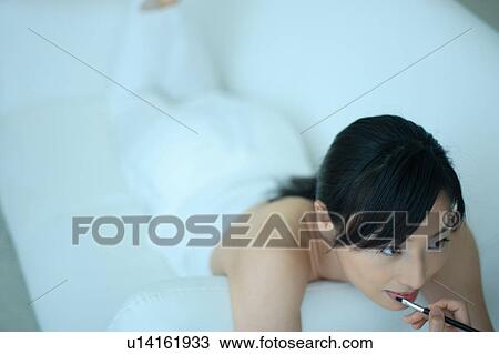 Stock Image - A young woman applying lipstick. Fotosearch
