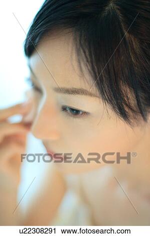 Stock Image - A young woman applying makeup, close-up. Fotosearch