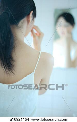 Picture - A young woman applying makeup, rear view. Fotosearch