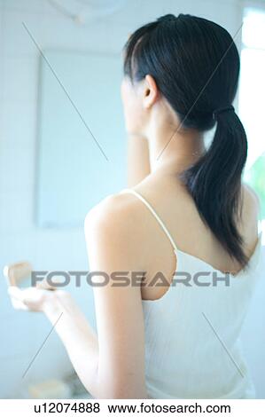 Stock Photo - A young woman applying makeup, rear view. Fotosearch