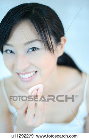 Stock Photo - A young woman applying makeup, smiling. Fotosearch