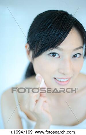 Stock Photo - A young woman applying makeup, smiling. Fotosearch