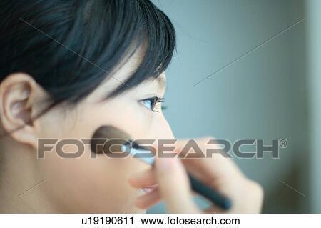 Stock Image - A young woman applying makeup with brush. Fotosearch