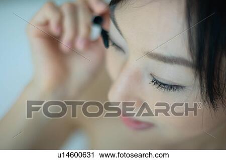 Stock Image - A young woman applying mascara, close-up. Fotosearch