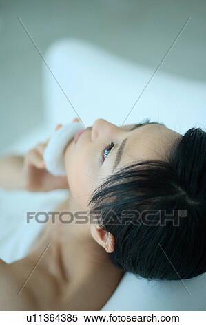 Stock Photography - A young woman looking up and applying makeup. Fotosearch
