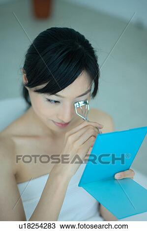 Stock Image - A young woman using eyelash curler. Fotosearch