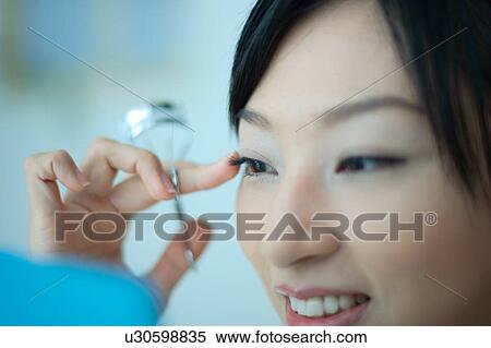 Stock Photography - A young woman using eyelash curler, close-up. Fotosearch