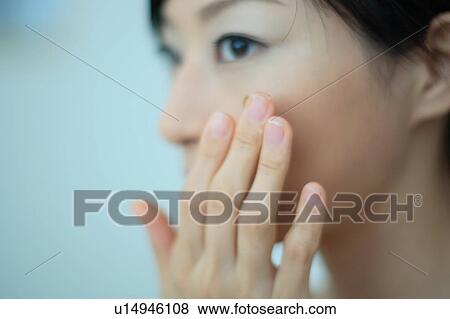 Stock Photo - Close-up of a young woman putting moisturizer to face. Fotosearch
