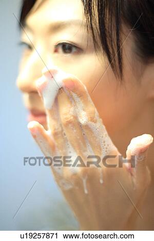 Stock Image - Close-up of a young woman washing face with soap. Fotosearch