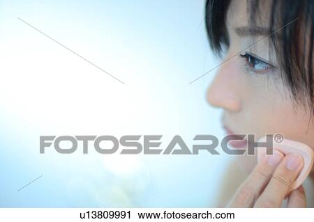 Stock Image - Profile of a young woman applying makeup, close-up. Fotosearch