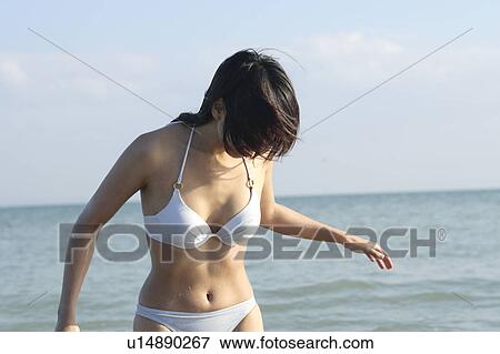 Stock Photo - A young woman in bikini playing with surf. Fotosearch