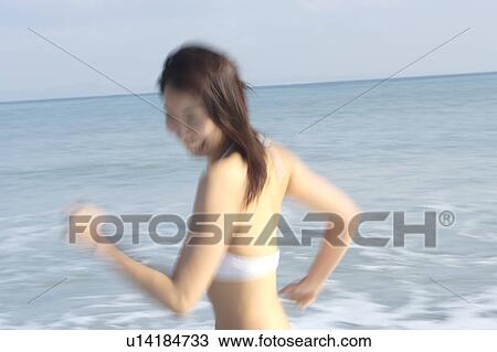 Stock Image - A young woman in bikini running at beach, blurred motion. Fotosearch
