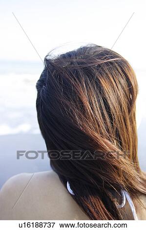 Stock Photo - A young woman in bikini sitting at beach, rear view, close-up. Fotosearch