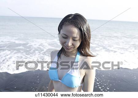 Picture - A young woman in bikini standing at beach. Fotosearch