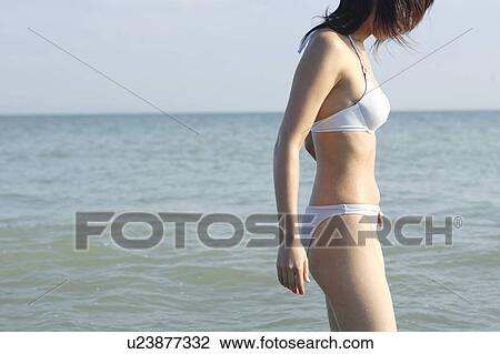 Stock Image - A young woman in bikini standing at beach. Fotosearch