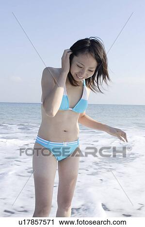 Stock Image - A young woman in bikini standing in surf. Fotosearch