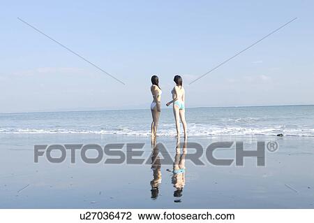 Two young women in bikini standing at beach, rear view View Large Photo Image Stock Image - Two young women in bikini standing at beach, rear view. Fotosearch