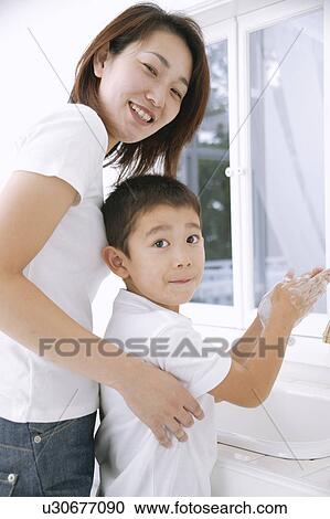 Boy washing hands with mother standing behind View Large Photo Image Stock Image - Boy washing hands with mother standing behind. Fotosearch