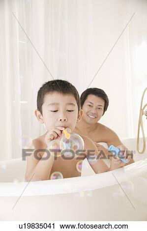 Stock Image - Father and son playing with bubbles in bathroom. Fotosearch