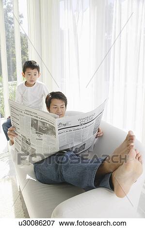 Stock Photo - Father reading newspaper in sofa. Fotosearch