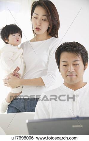 Stock Photograph - Father using computer with mother standing behind. Fotosearch