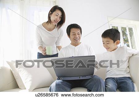 Stock Photograph - Father using computer with son and mother looking. Fotosearch